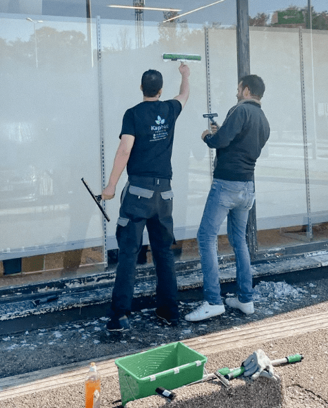 Deux travailleurs de chez Kapnet nettoyant des vitres d'un magasin.