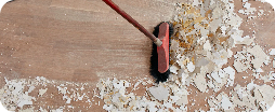 Balai ramassant des débris de chantiers après travaux sur un parquet en bois.